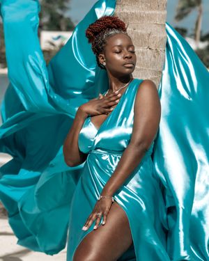 Turquoise silk dress flows elegantly against a palm tree on a tropical beach setting.