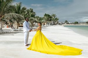 Stunning yellow gown with long train flows on white sand beach with palm trees.