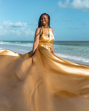 Gold satin dress twirls against ocean waves and blue sky.