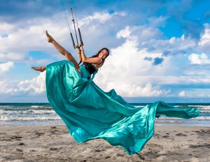 Teal flowing dress catches wind during beach kiteboarding photoshoot.