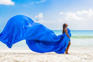 A royal blue flowing dress catches the ocean breeze on a sunny beach.