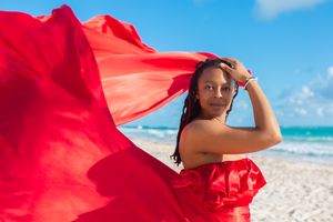 Flowing red fabric dress billows dramatically against a tropical beach backdrop on a sunny day.