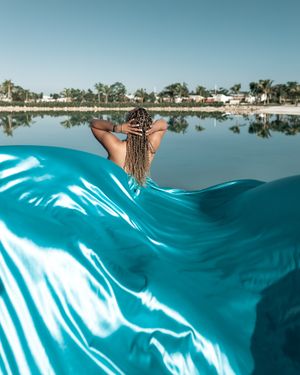 A turquoise fabric flows dramatically over water with a serene lakeside reflection.