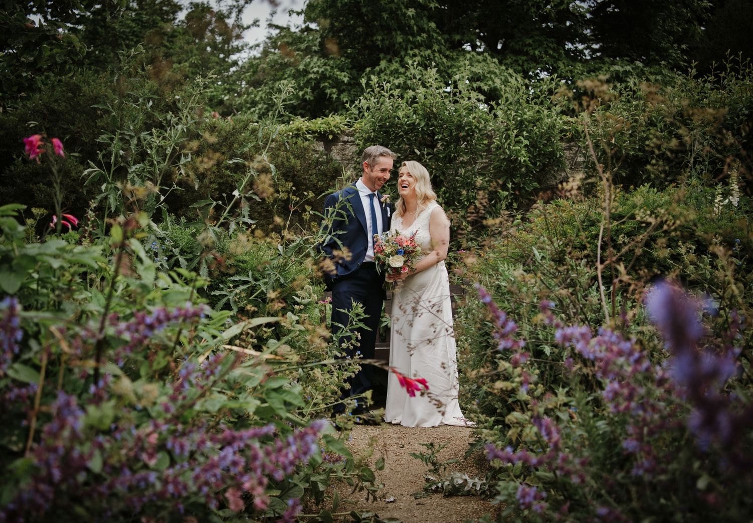 A bride and groom sit together during their wedding ceremony, the groom in a navy suit and bride in a white gown with veil.