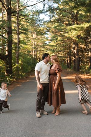 A couple shares a tender moment on a forest path while two young children play around them on a sunny day.