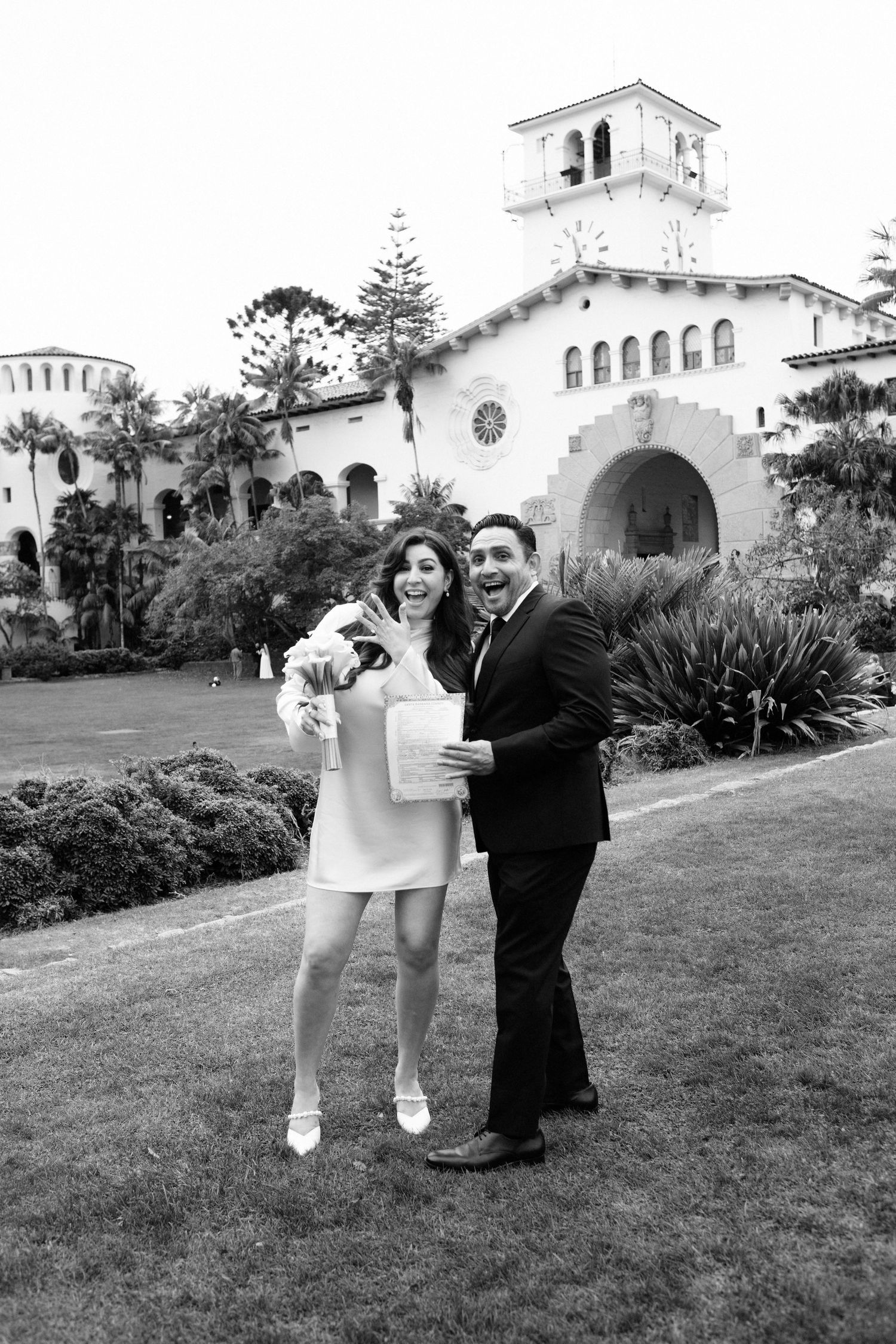 Happy couple posing in front of Santa Barbara Courthouse on their wedding day in black and white photo.