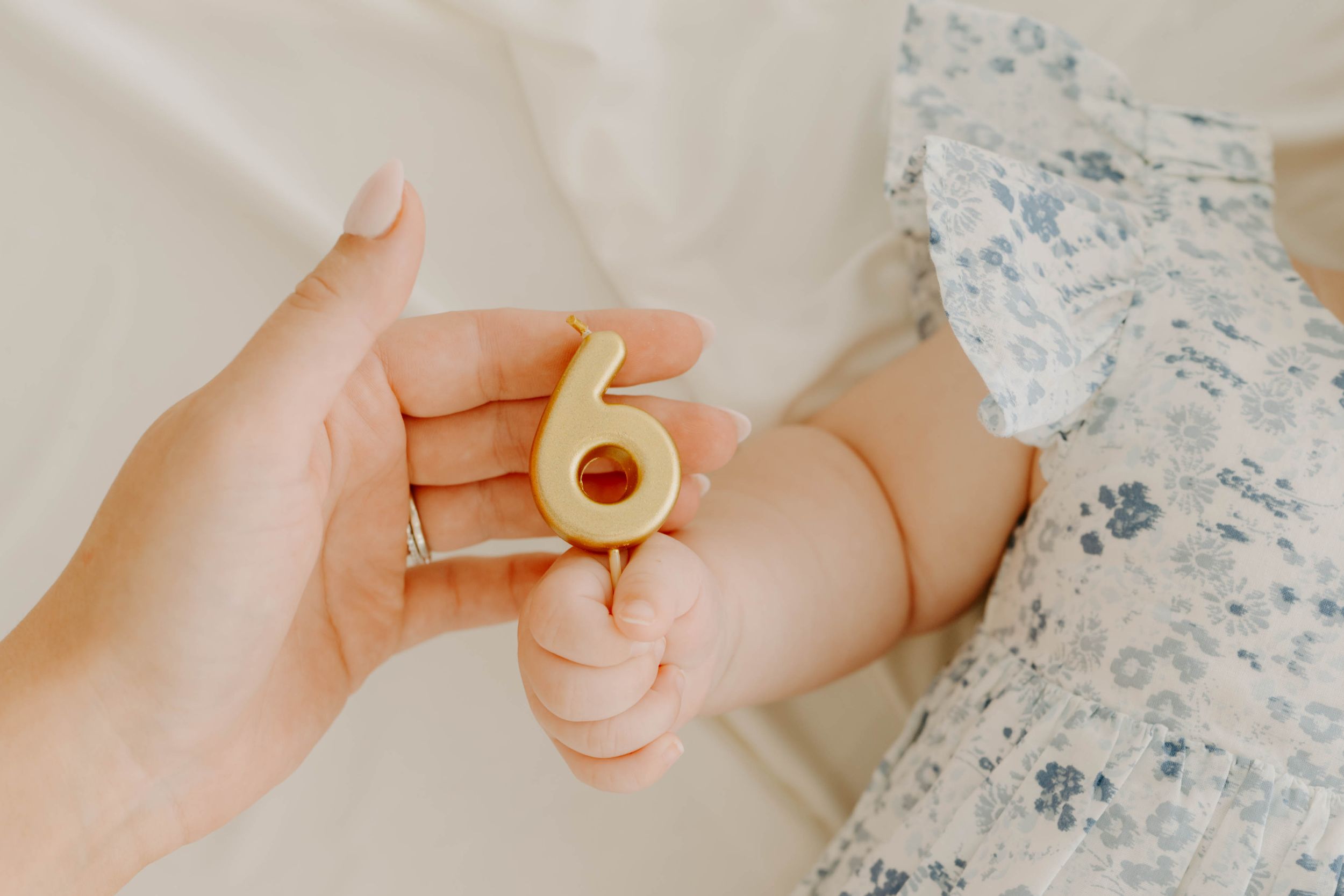 A parent holds a number 6 candle as a baby grasps it, celebrating a 6-month milestone.