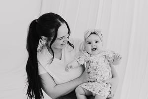 Black and white photo of a smiling mother holding her happy laughing baby girl in a floral outfit.