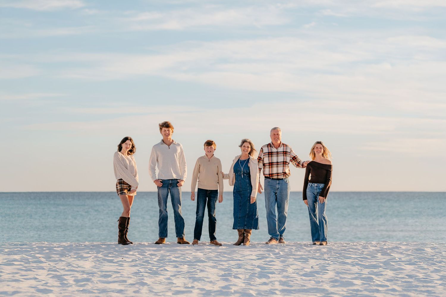 Family of eight poses together on a sandy beach at sunset, dressed in coordinating neutral and white outfits.