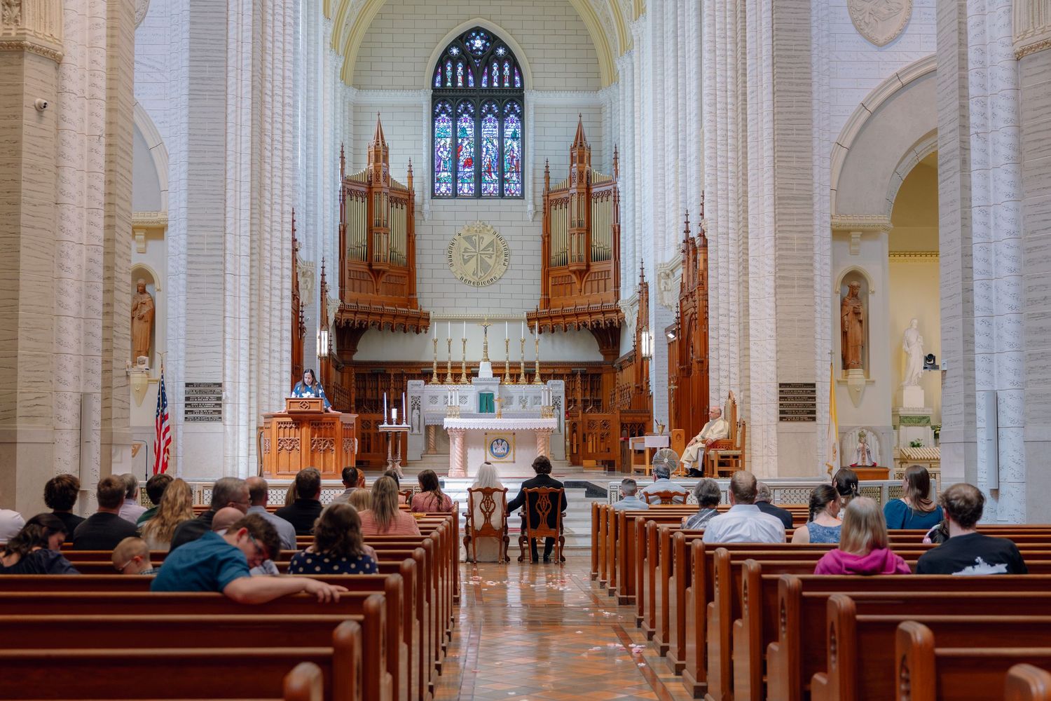 Interior of a grand church with wooden pews, ornate pipe organ, and stained glass windows during a service.