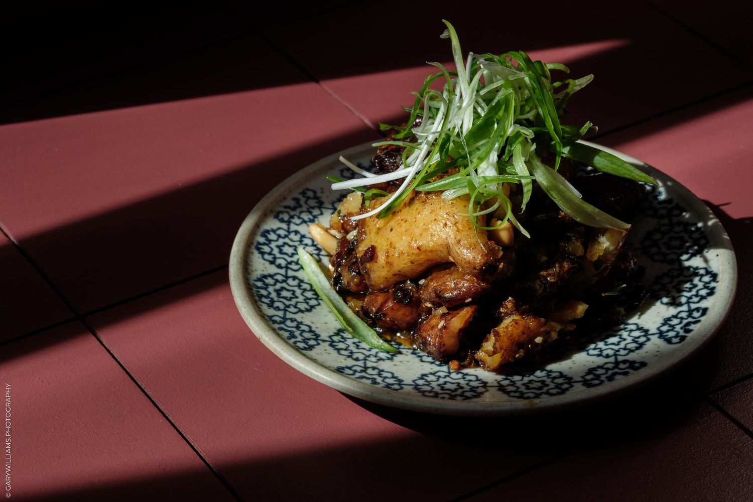 A decorative plate with crispy braised pork belly topped with fresh green herbs, served on a red wooden table.