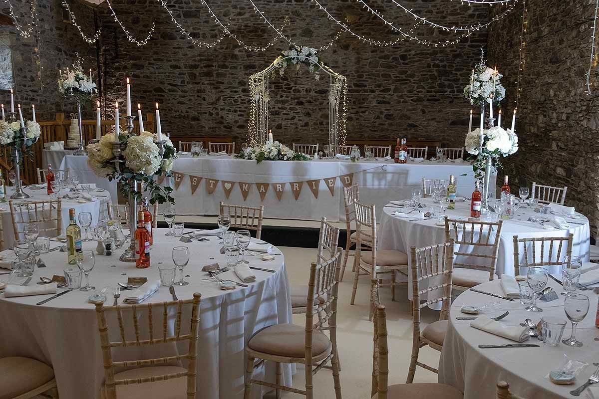 Elegant wedding reception at New House Farm wedding venue with round tables, chiavari chairs, floral arch, and fairy lights.