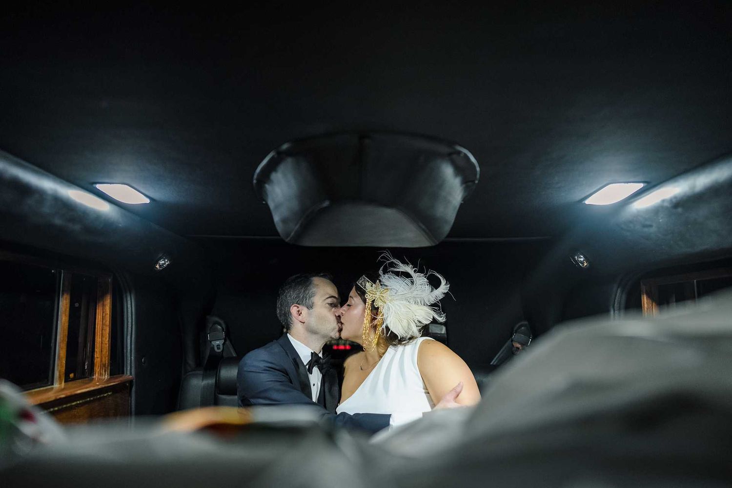 Bride and groom sharing a romantic kiss inside a dark limousine on their wedding day at the view wedding venue
