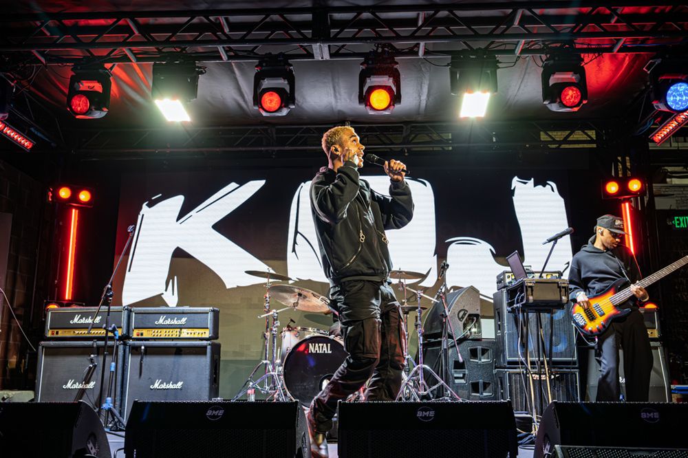 Rock band performing live on stage with Marshall amps, dramatic lighting, and singer holding microphone.