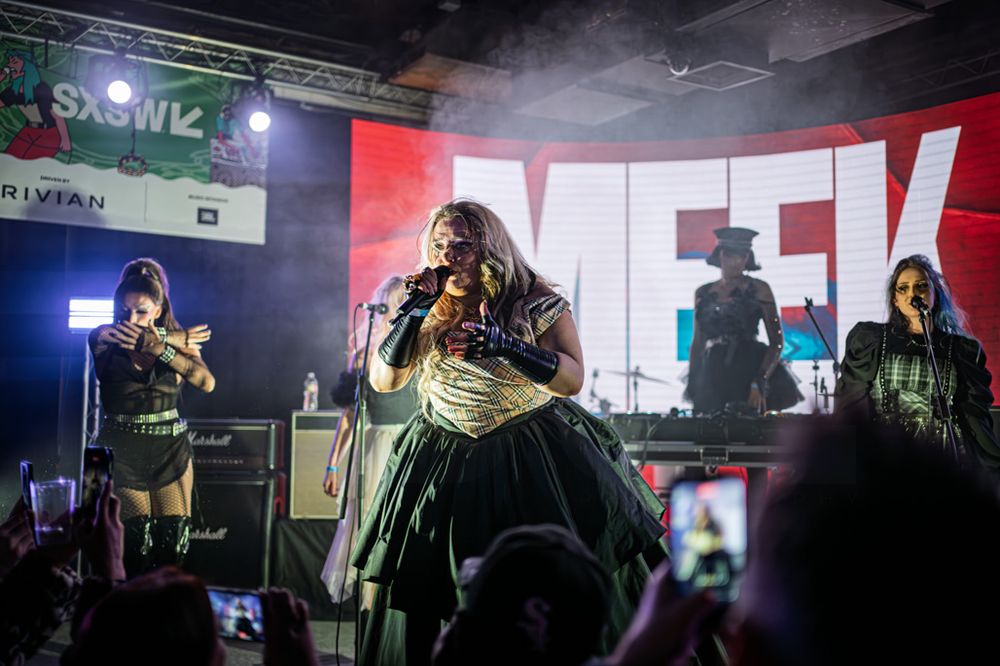 Plus-size singer performs on SXSW stage in green gown with band members under colorful lights.