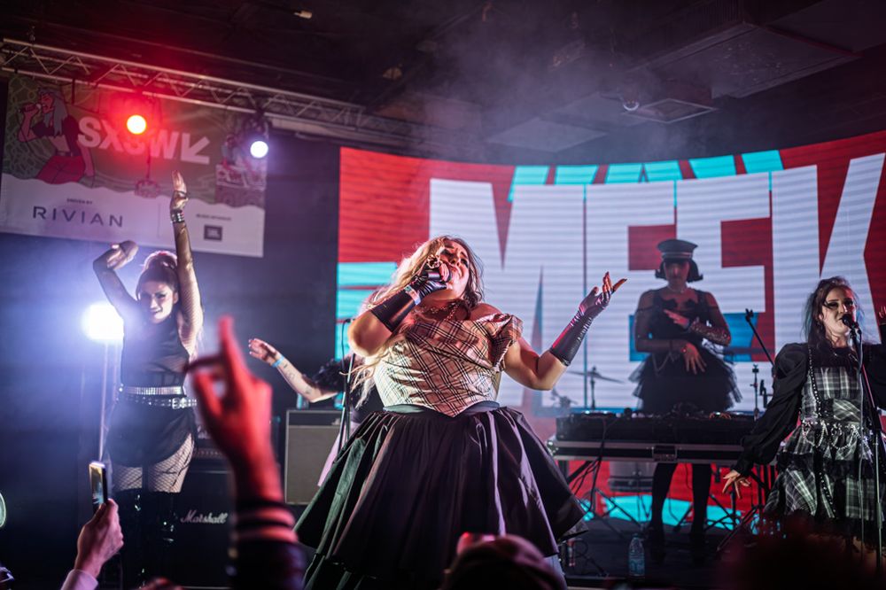 Live performer on stage at SXSW music festival with band members and colorful LED backdrop lighting.