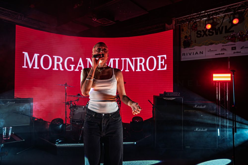 Morgan Munroe performs on stage in front of a red-lit backdrop displaying her name at a live concert event.