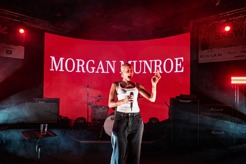 Morgan Munroe performing on stage in front of a red LED backdrop at a live concert event.