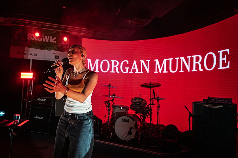Morgan Munroe performing live on stage, singing into a microphone with a red-lit backdrop displaying her name.