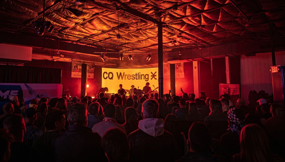CQ Wrestling event in a dimly lit venue with red lighting, crowd watching performers on a yellow-lit stage.
