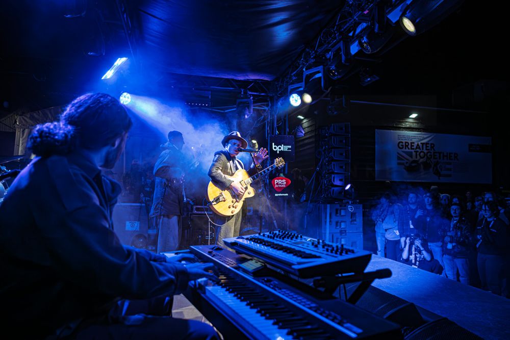 Live band performs on a blue-lit stage with guitarist and keyboard player in an intimate music venue.