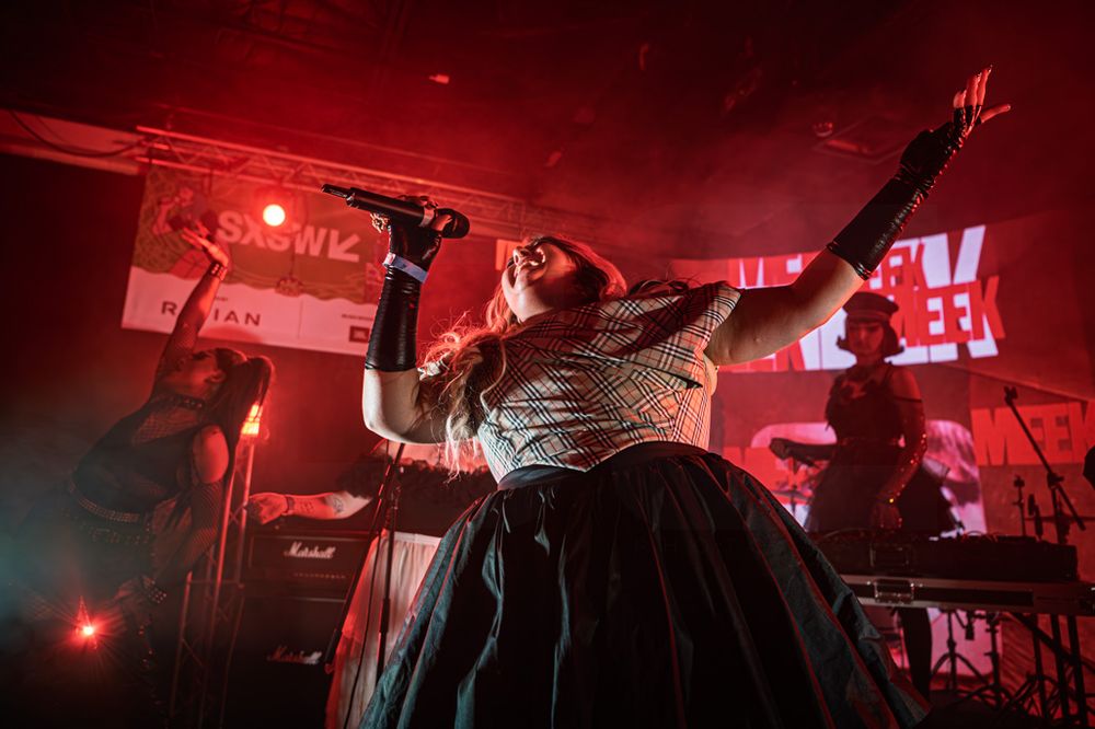 Female vocalist in a black ball gown performs passionately on a red-lit stage at a live concert.
