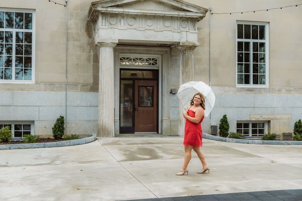 Woman in red dress holding white parasol umbrella walking in front of elegant stone building entrance.