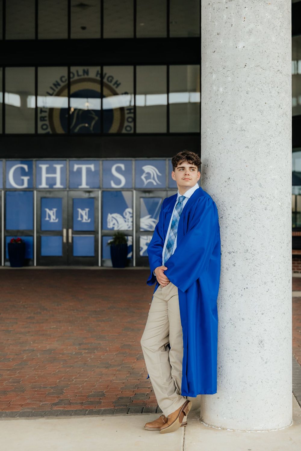 Young man in blue graduation gown leaning against a column outside North Lincoln High School.