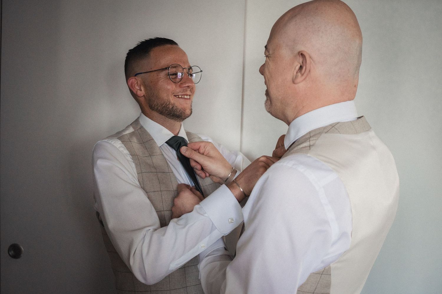 Two men in vests adjusting neckties while getting ready for a formal event or wedding ceremony.