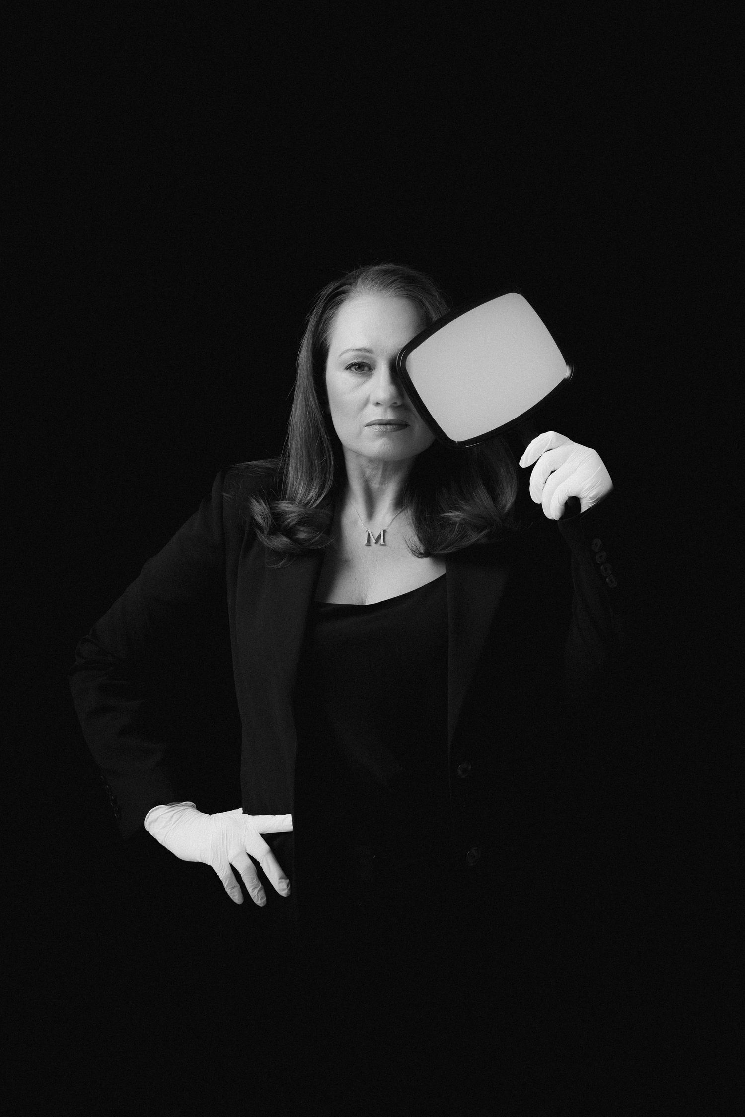 Woman in white blazer and trousers poses on black sofa wearing strappy wedge sandals in bright modern room.