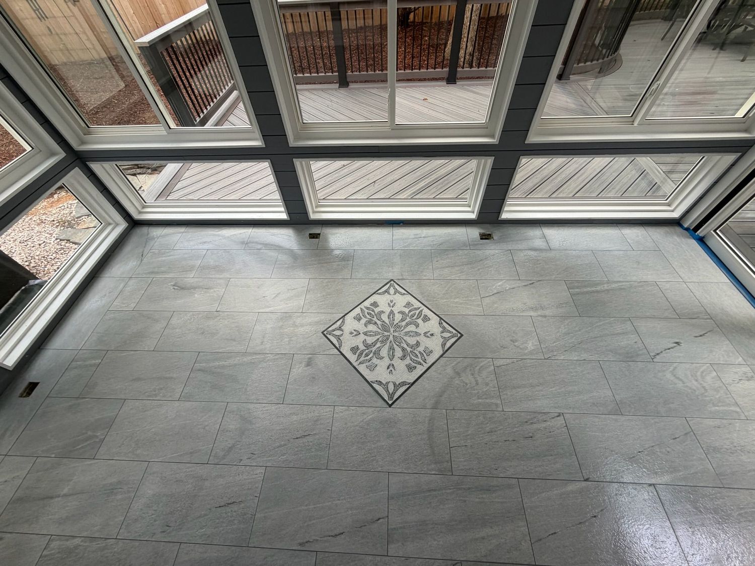 Sunroom with gray tile floor featuring decorative mosaic centerpiece and large windows.