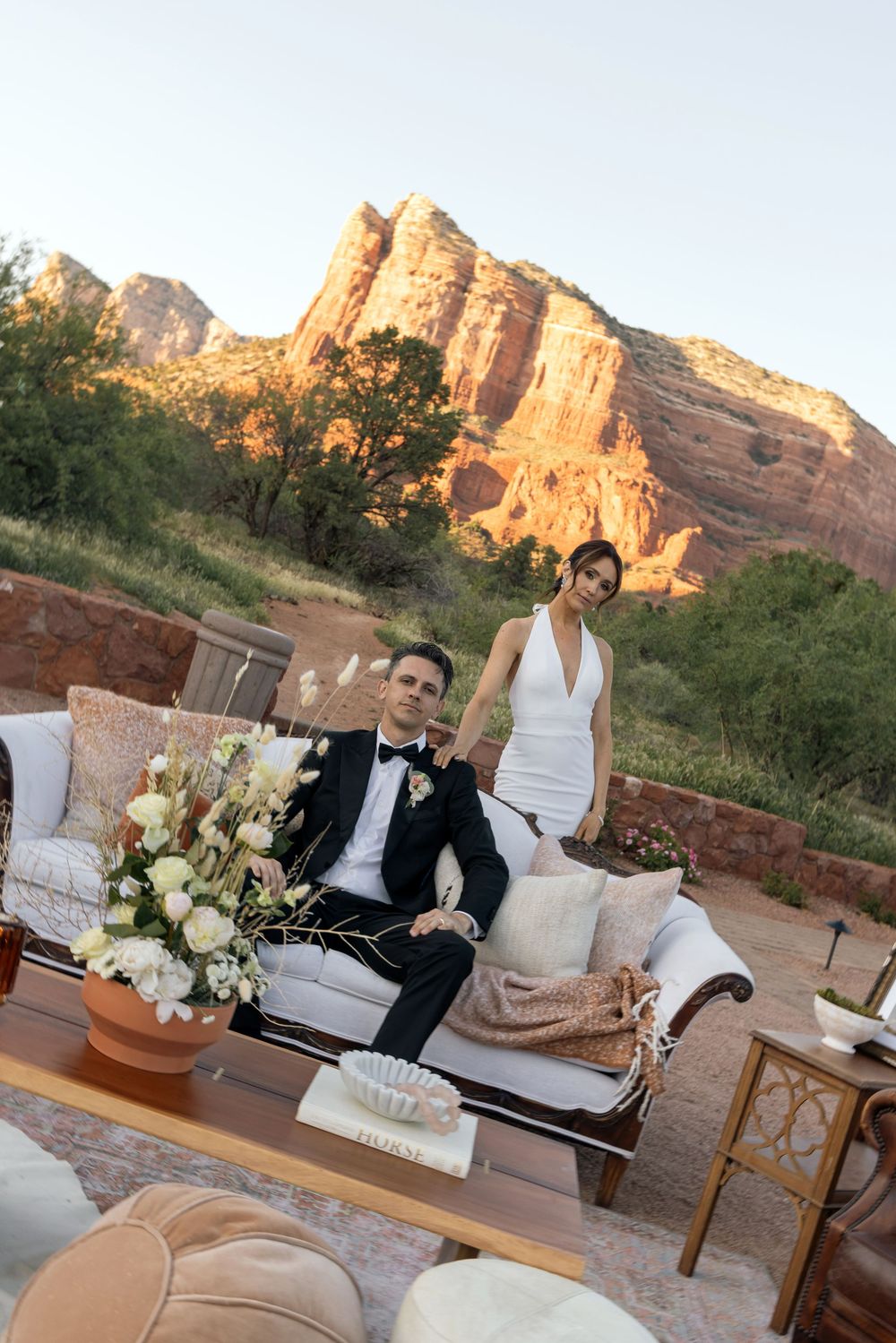 Bride and groom pose at outdoor lounge with red rock Sedona backdrop at sunset wedding reception.