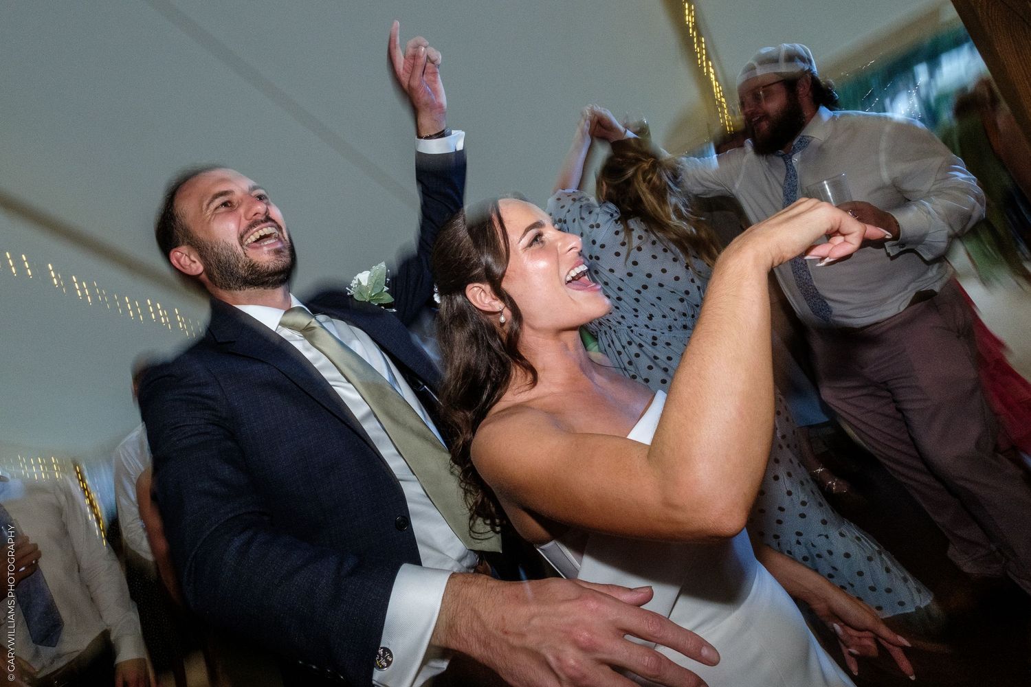 Bride and groom dancing joyfully at wedding reception under a white tent.