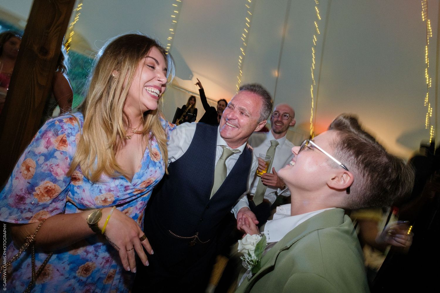 Guests laughing and celebrating at a wedding reception inside a decorated tent with string lights.