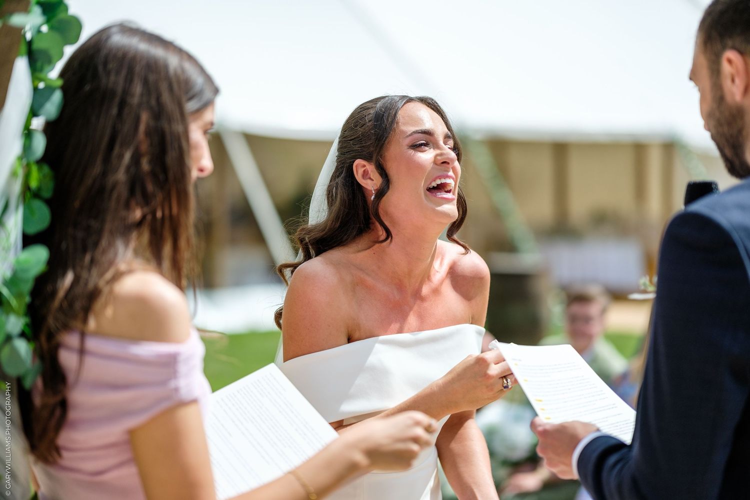 Emotional bride in white strapless gown reciting wedding vows outdoors at tent ceremony.