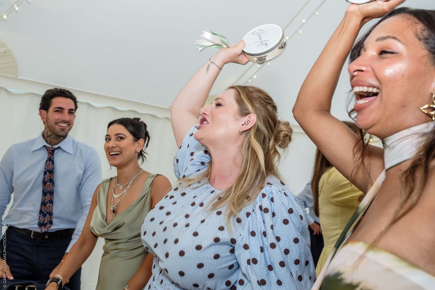 Women laughing and dancing at a lively wedding reception party, one drinking from a decorative bottle.
