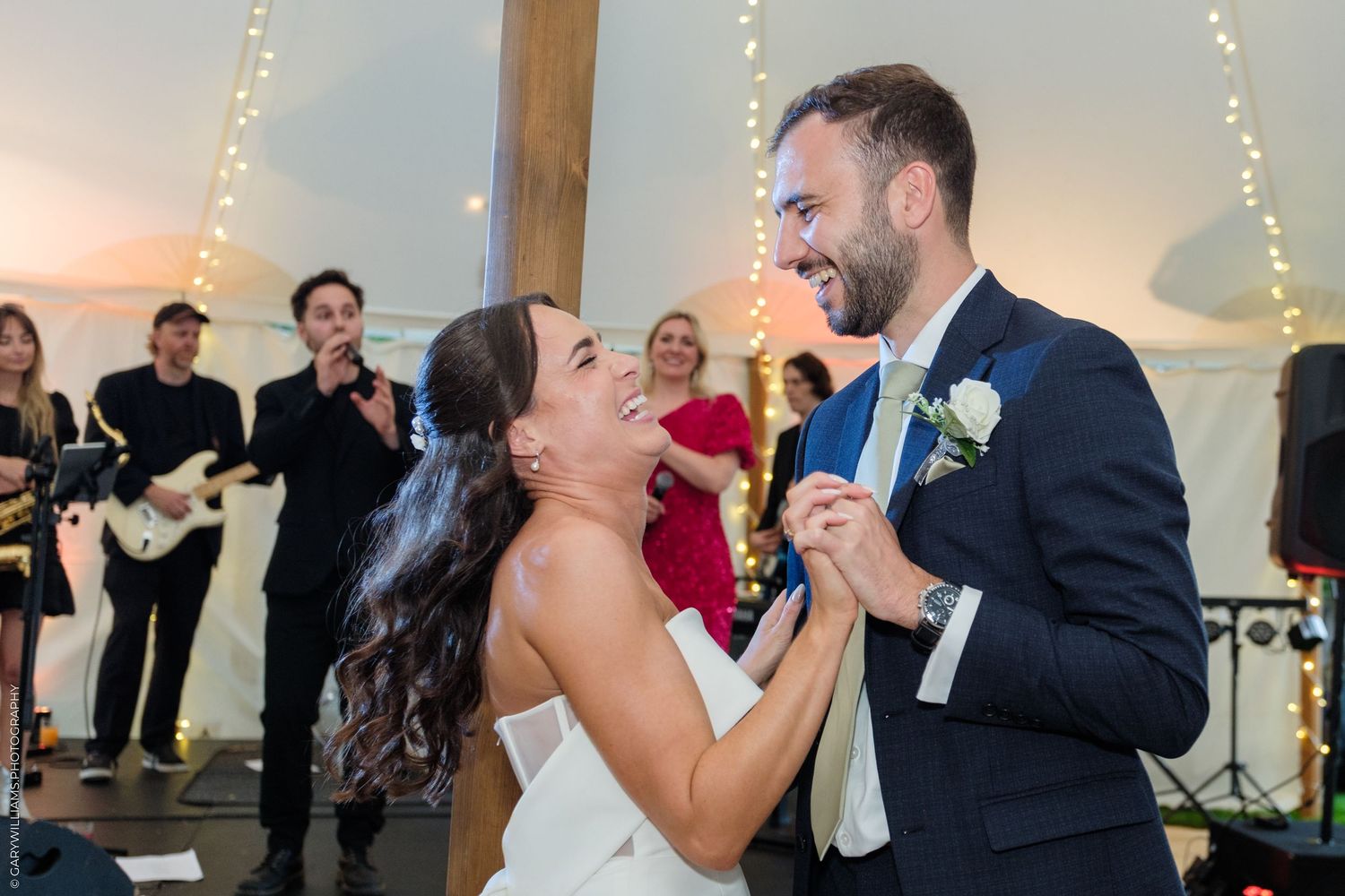 Bride and groom share first dance at wedding reception with live band performing in background.
