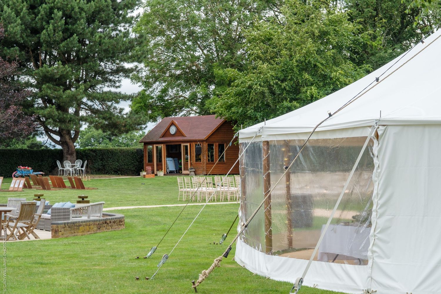 Elegant white bell tent beside a rustic wooden cabin in a lush green garden at a countryside wedding venue.