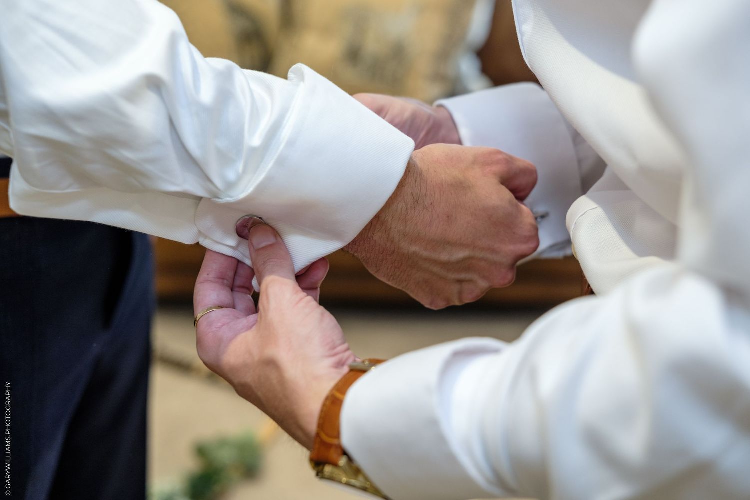 A groomsman fastens the cufflink on the groom's white dress shirt before the wedding ceremony.