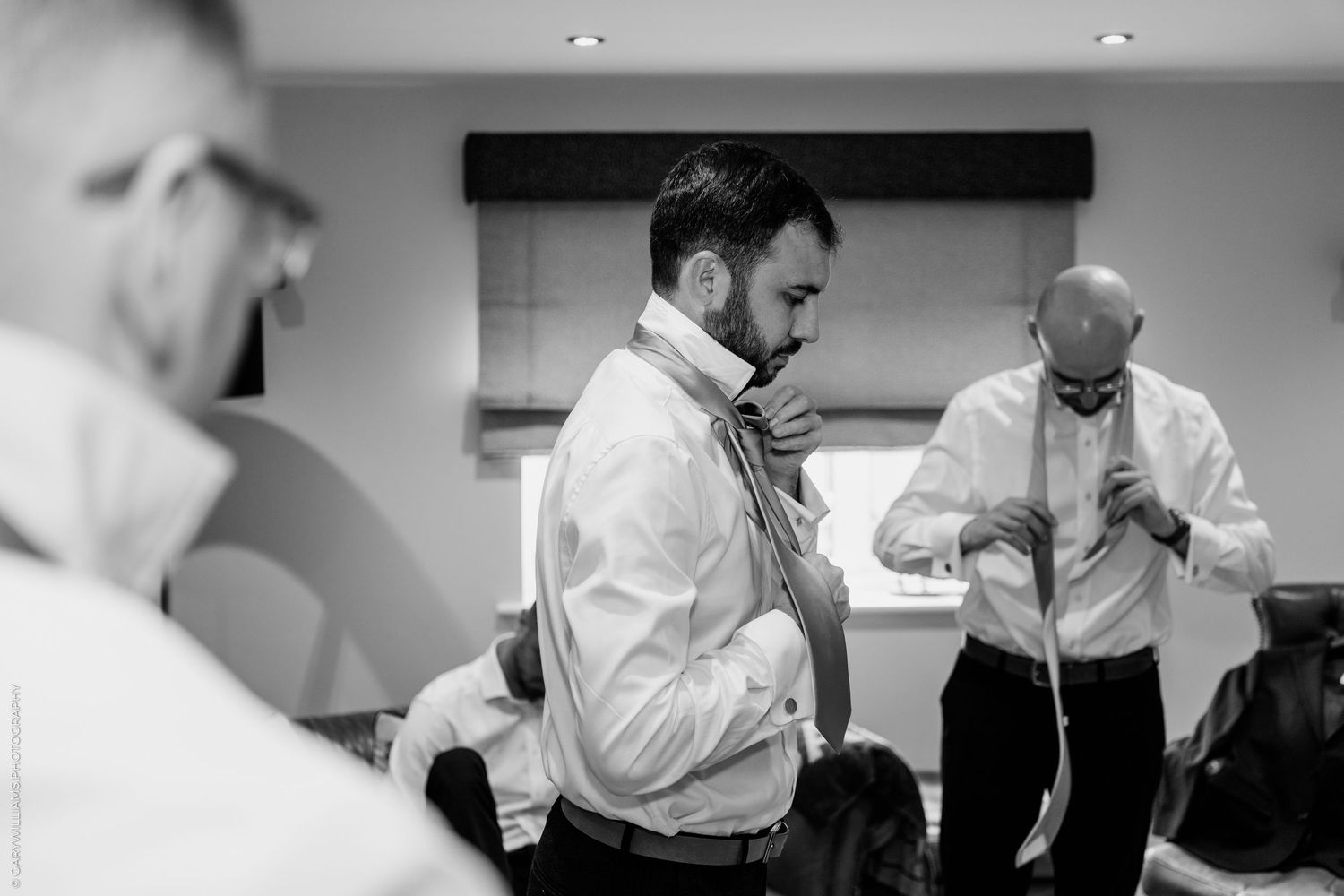 Groom and groomsmen adjusting ties while getting ready before a wedding ceremony in black and white.