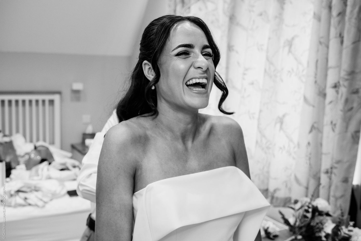 Black and white photo of a laughing bride in a strapless wedding dress during bridal preparations.