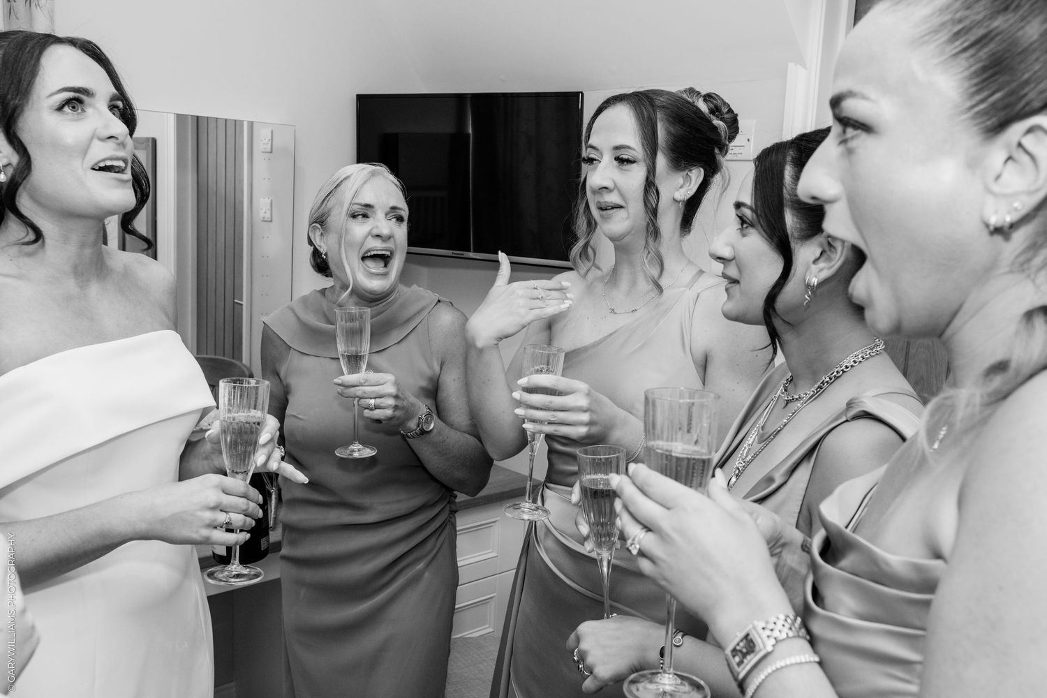Bridesmaids laughing and toasting with champagne glasses in black and white wedding photo.