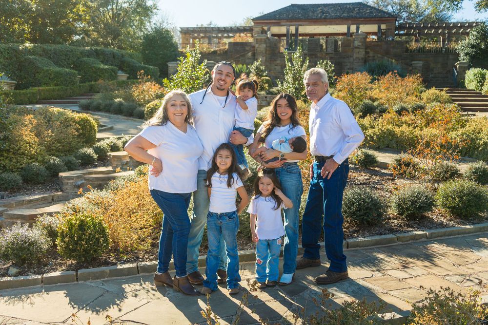 Family of seven posing together in a lush garden setting, wearing matching white shirts and jeans on a sunny day.