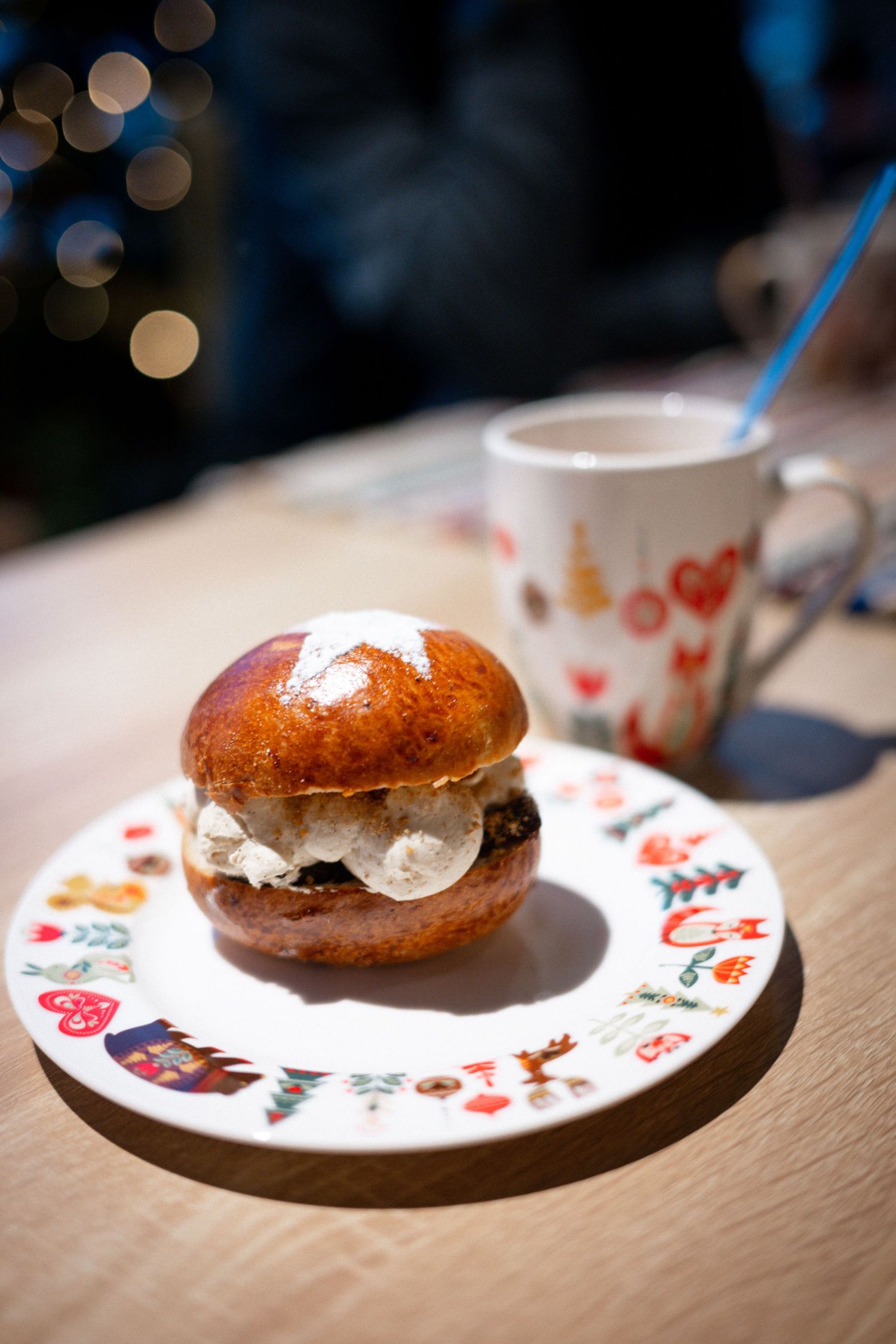 A cream-filled brioche bun on a festive Christmas plate beside a holiday mug on a wooden table.