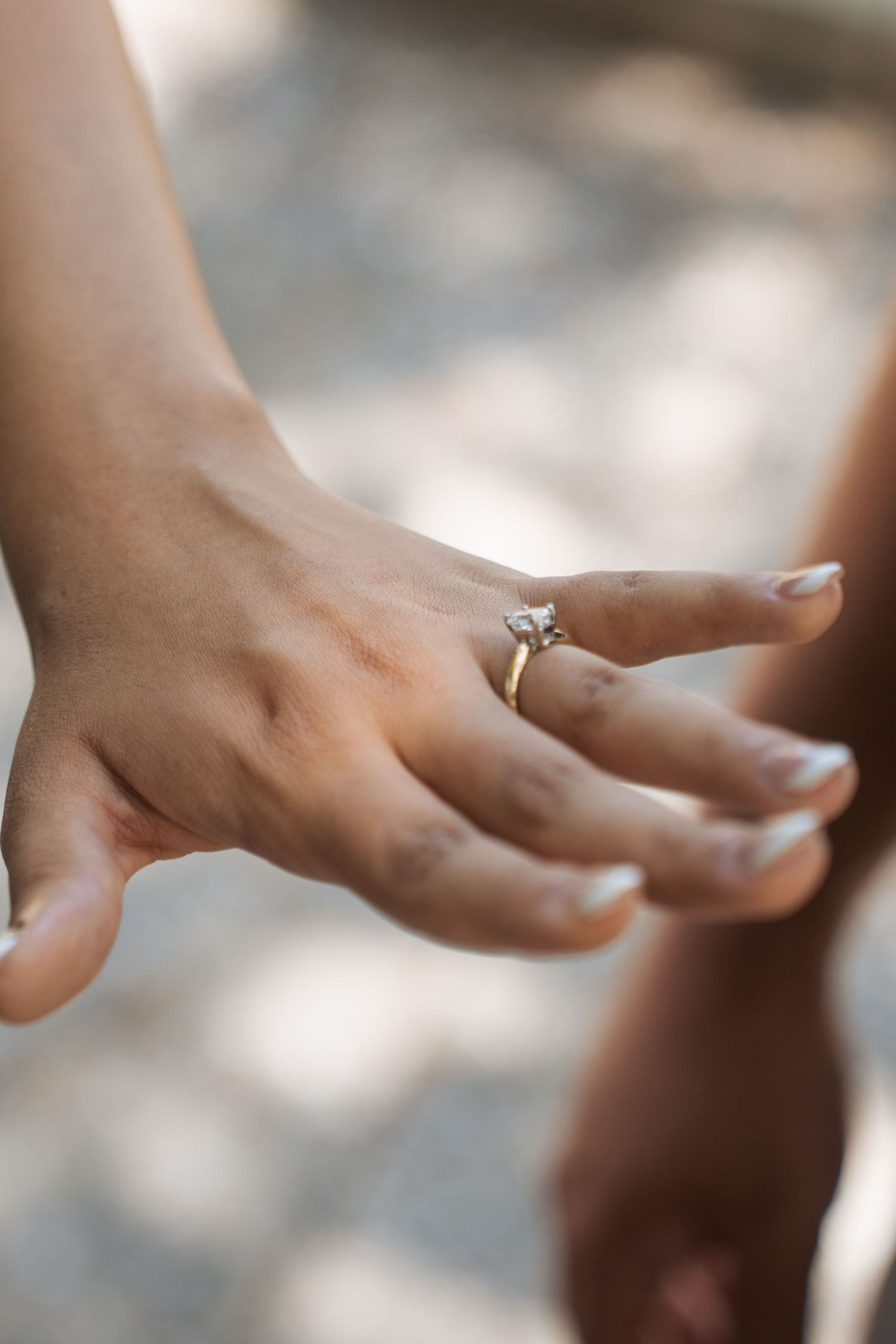Two hands holding together, one adorned with a gold solitaire diamond engagement ring, captured in soft natural light.