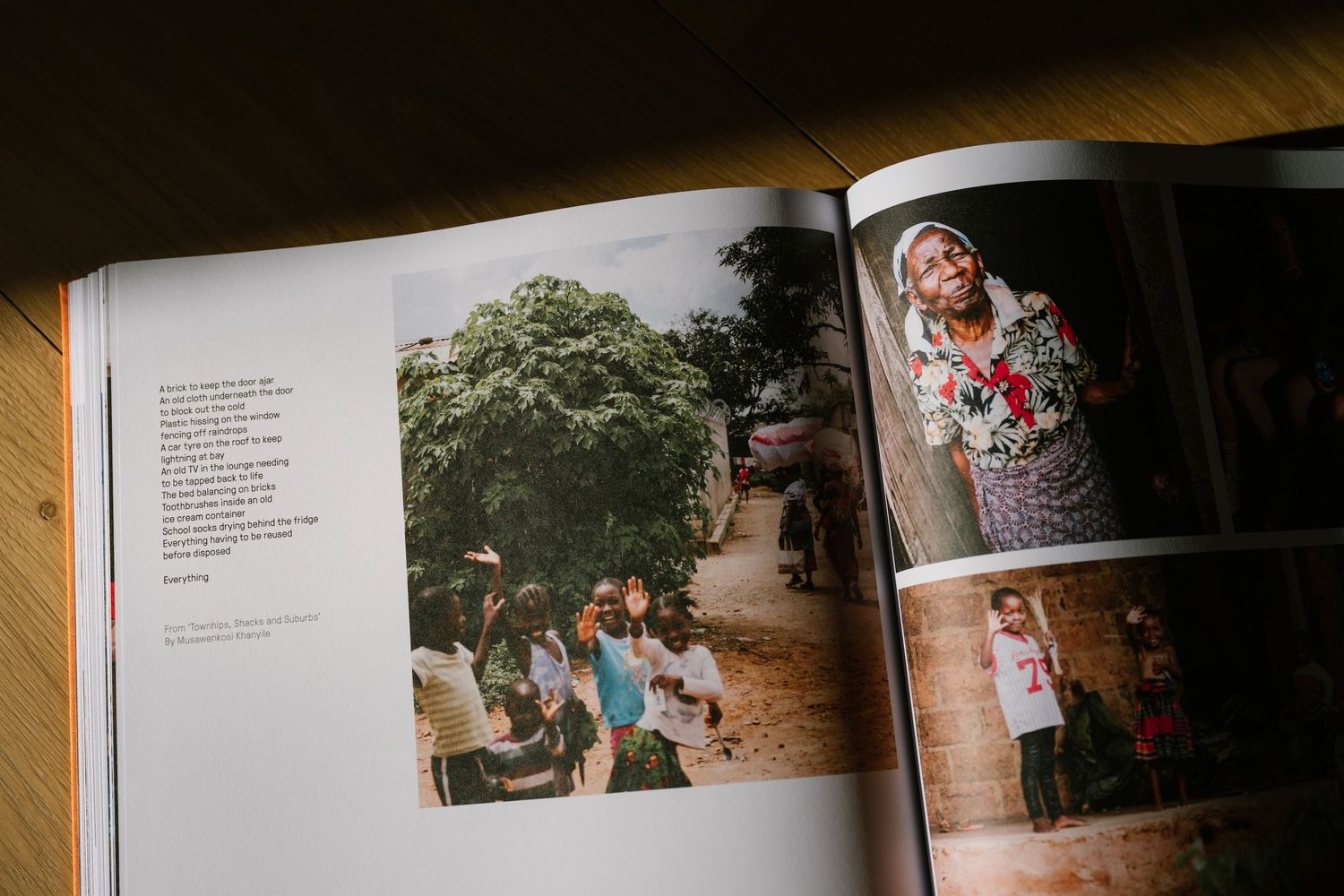 Open photography book on wooden table showing African community photos and portrait of woman in colorful floral dress.