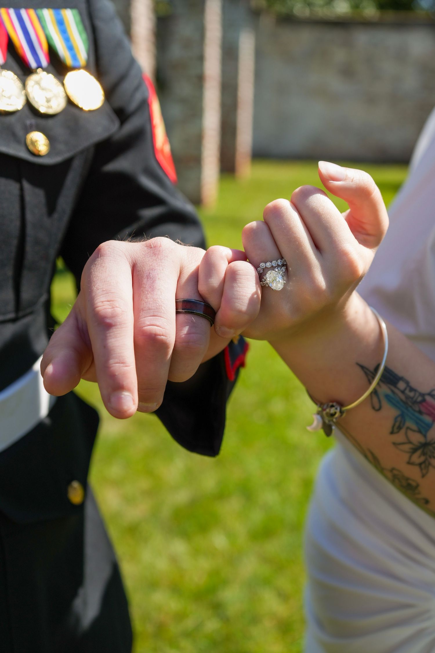 Close-up of couple holding pinkies, woman wearing diamond engagement ring with tattoo visible.