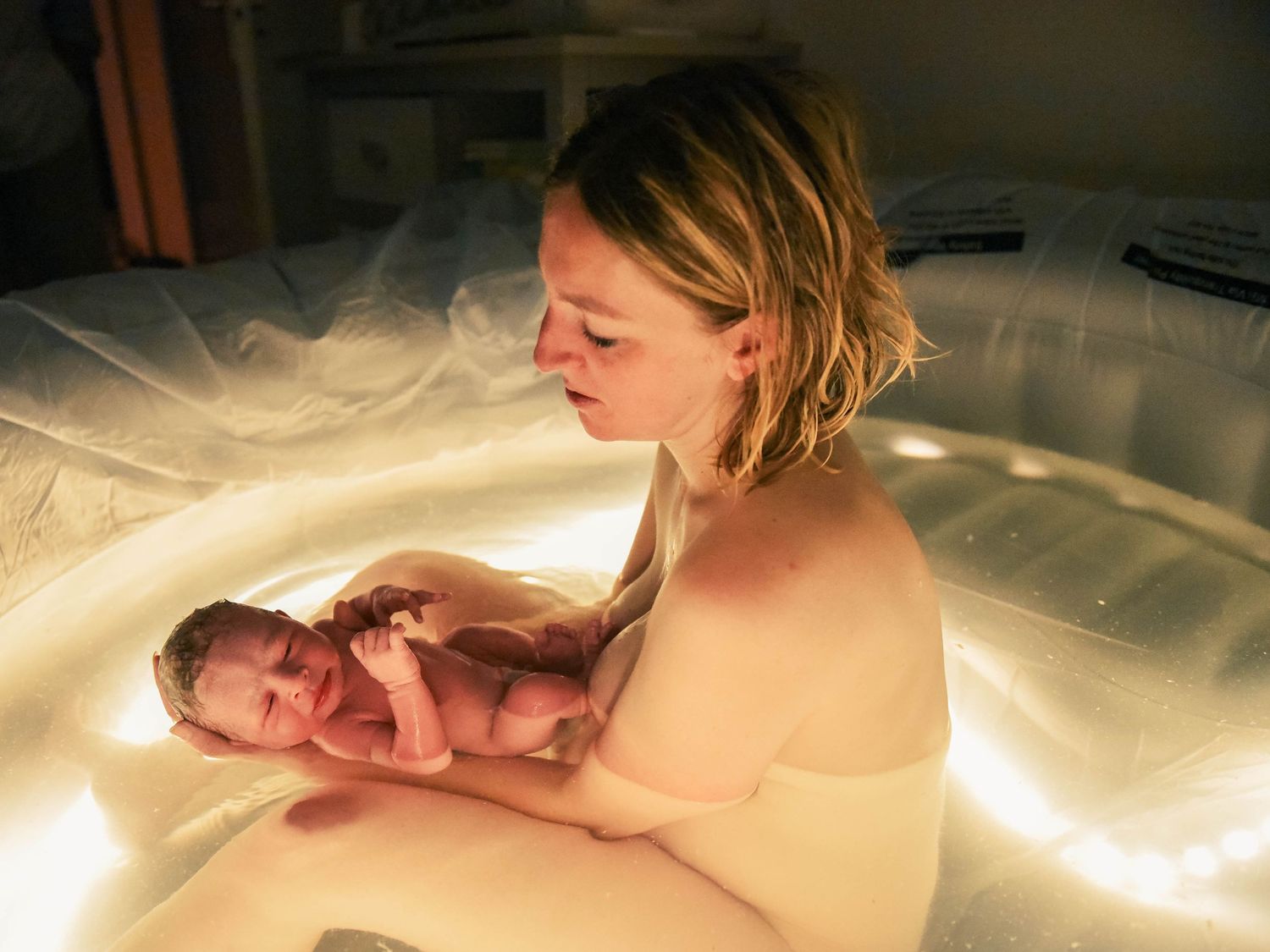 A mother holds her newborn baby in a birthing pool during a water birth.