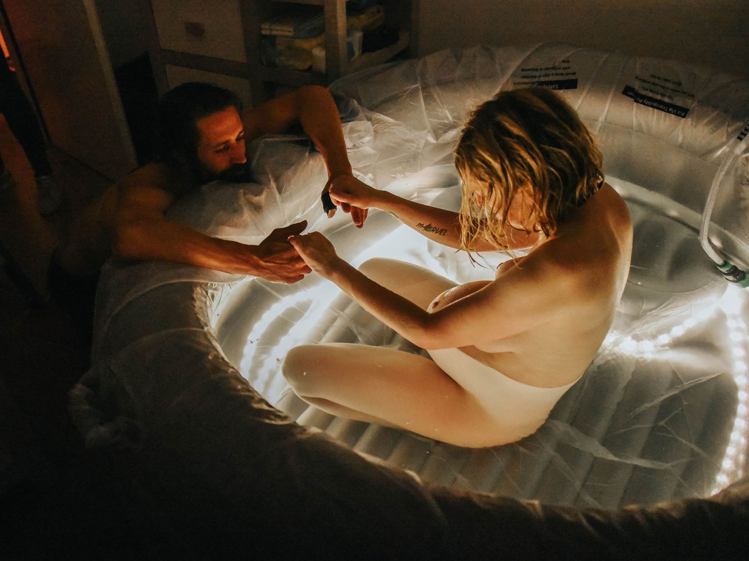 A couple relaxes together on a glowing inflatable bed in a dimly lit room.