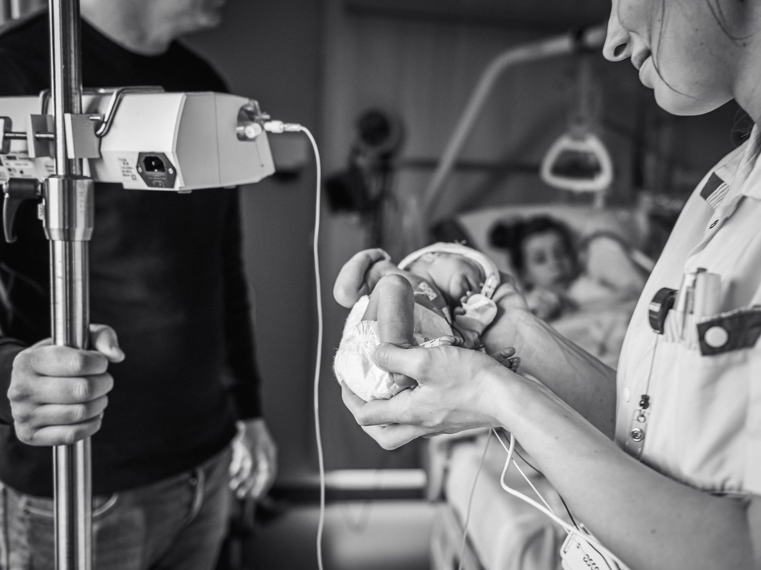 Black and white photo of a nurse carefully holding a premature newborn baby in a hospital NICU ward.